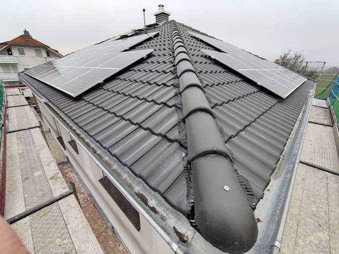 Dach mit Solarmodulen und Schornstein.